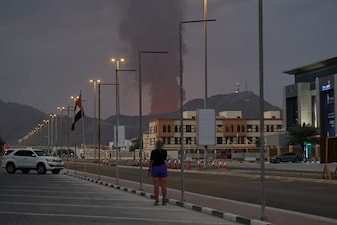 A woman looks at a tall plume of black smoke ascends following an explosion in the Fujairah industrial zone on March 3, 2026. (AFP)