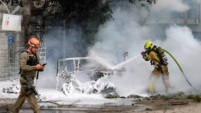 A firefighter extinguishes a blaze in a vehicle following a projectile impact from an Iranian strike in southern Tel Aviv on March 15, 2026.- AFP