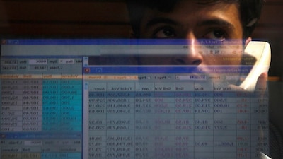 A computer screen displaying stocks is reflected in the window of a booth, where a man is monitoring the market. File image/Reuters