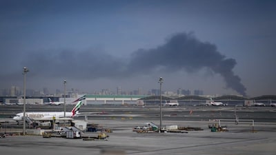 A plume of smoke caused by an Iranian strike is seen in the background as Emirates planes are parked at Dubai International Airport after its closure in Dubai, United Arab Emirates. (Photo: AP)