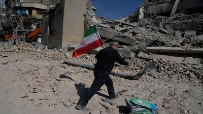 A man carries an Iranian flag to place on the rubble of a police facility struck during the US–Israeli military campaign in Tehran, Iran. AP