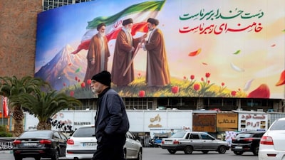 A man walks near a banner displayed at Valiasr Square in central Tehran, depicting Iran's late supreme leader Ayatollah Ruhollah Khomeini  watching as his successor the late Ayatollah Ali Khamenei hands over a national flag to his son and new supreme leader Mojtaba Khamenei. AFP