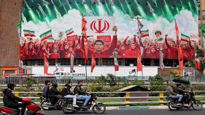 Motorists ride scooters near a large political banner, depicting missiles being fired behind Iranian demonstrators in solidarity with the government, at Valiasr Square in Tehran. (Photo: AFP)
