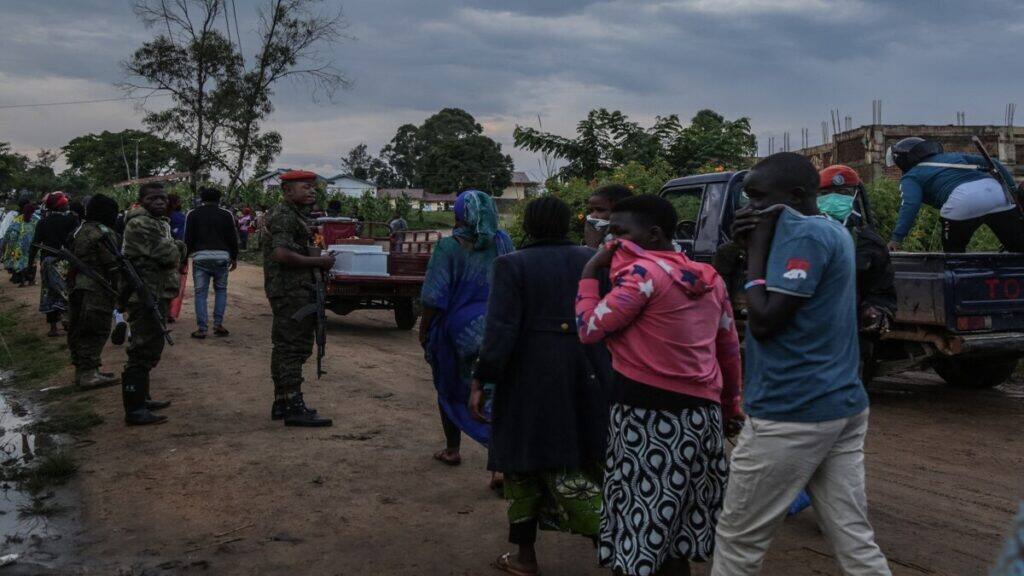 Pederstrians cover their mouth and nose as they walk past a convoy ready to escort the body of a patient deceased at the hospital in Rwampara towards the cemetery. File/AFP