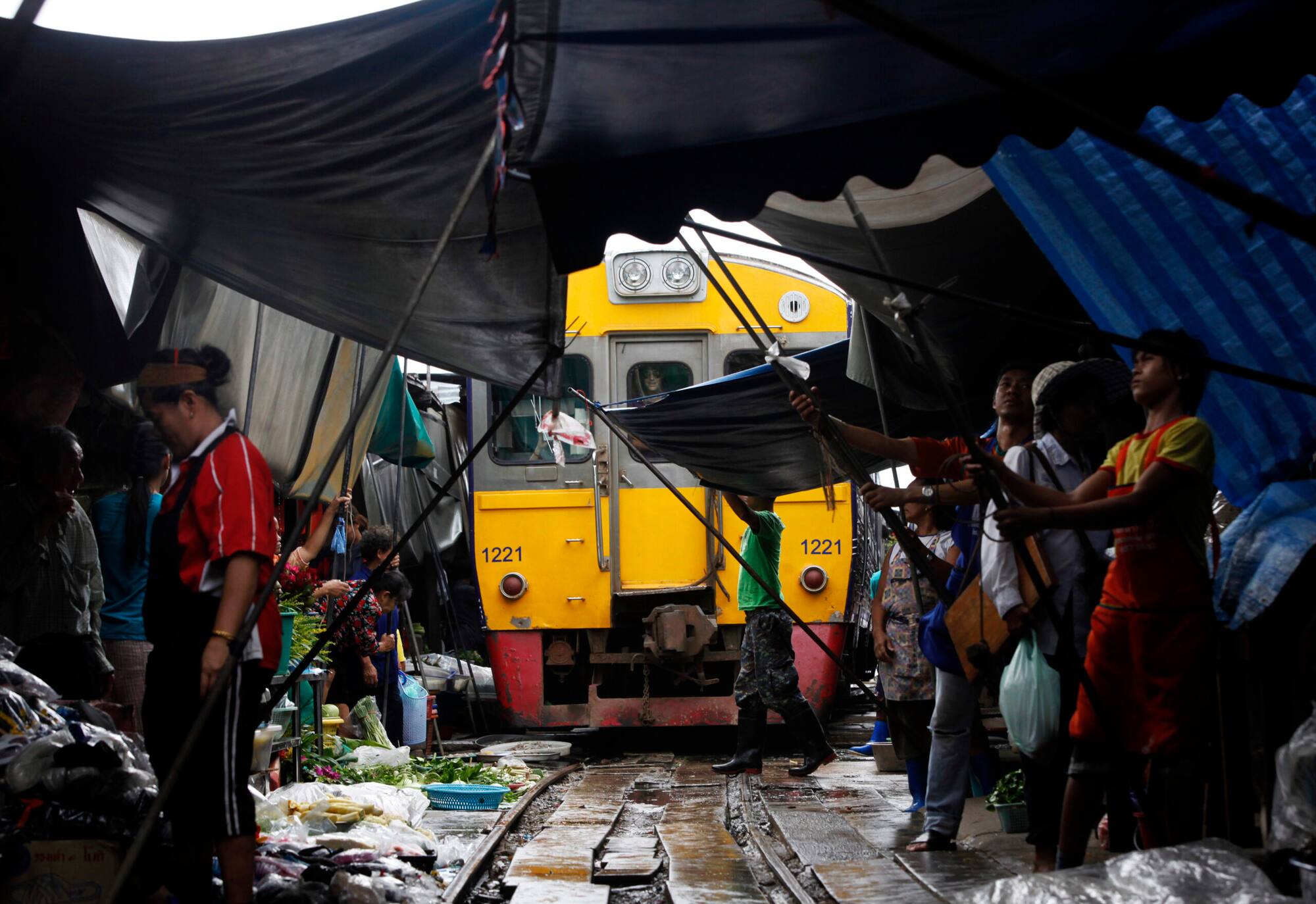 Thai vegetable market vendors pull back awnings and their produce off a railway track to allow a cross-country train to dissect through the middle of the town of Maeklong