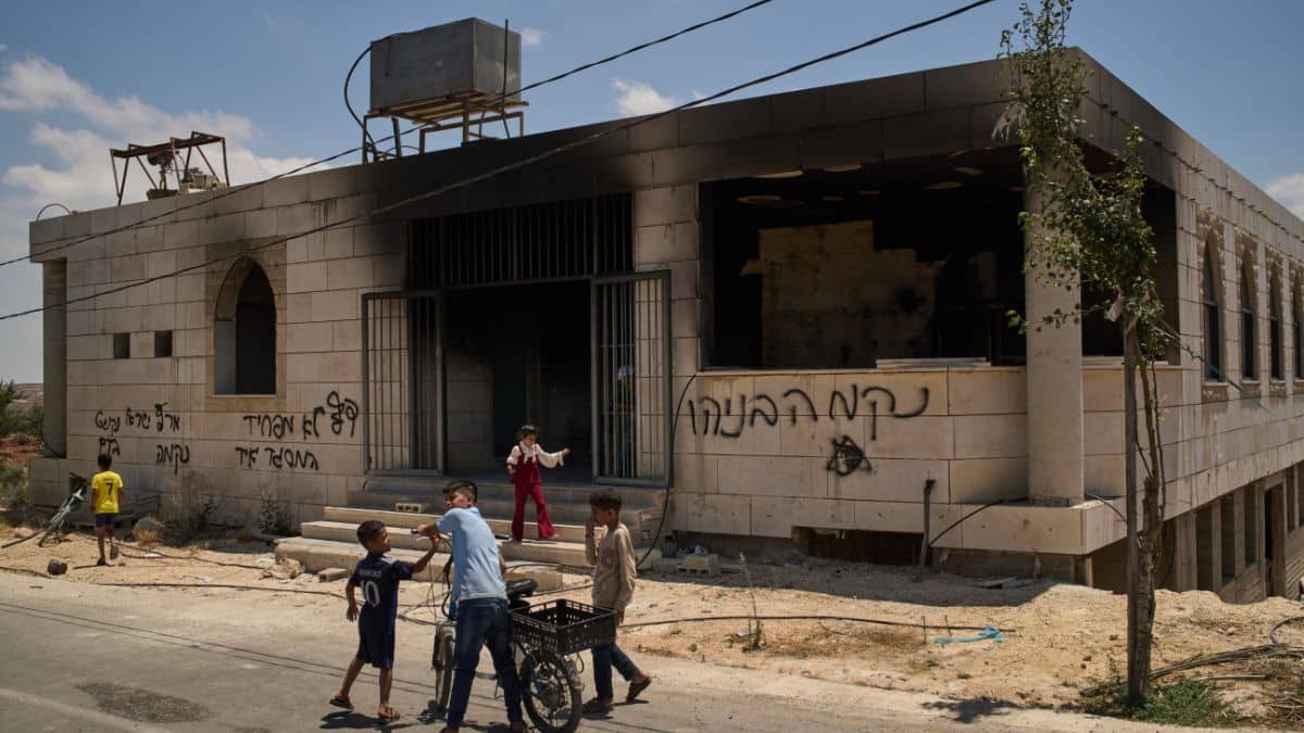 Children stand outside a mosque that was burned during an attack by Israeli settlers in the West Bank village of Qusra on