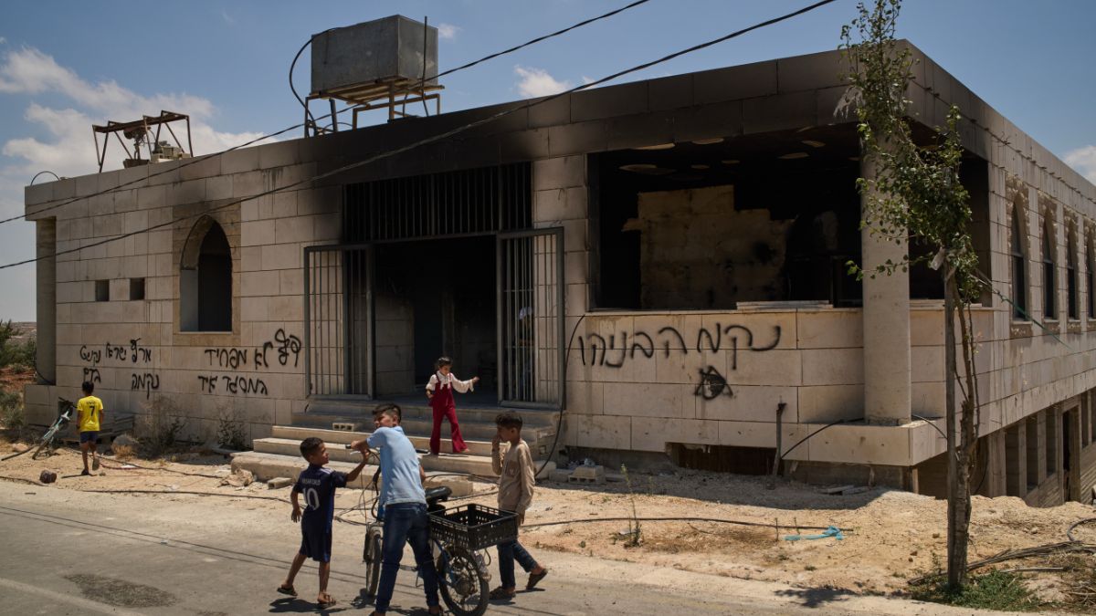 Photo: firstpost.com Children stand outside a mosque that was burned during an attack by Israeli settlers in the West Bank village of Qusra on