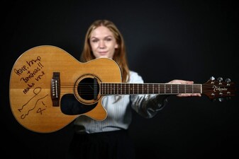 A member of staff poses with an autographed Takamine FP460SC acoustic guitar from OASIS guitarist Noel Gallagher used during their 1996 appearance on 'MTV Unplugged', during a preview by entertainment memorabilia auction house Propstore in central London on September 23, 2026. AFP