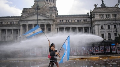 People hold Argentine flags while being sprayed with water from a water cannon during a demonstration demanding that the government of Argentine President Javier Milei comply with a law updating funding for public universities, in Buenos Aires, on October 15, 2026. AFP