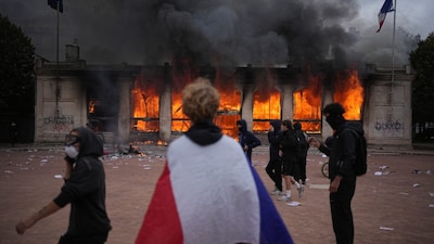 A protester wraps a French flag around them in front of the burning tourism office during a demonstration against rising living costs and in solidarity with students’ grievances in Lyon, France on Saturday (October 17). AP