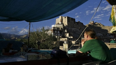 A tourist sits on a roof top restaurant with a view of Leh Palace in Leh. Tourism is booming in the Himalayan towns but they bring their own set of problems. File image/AFP