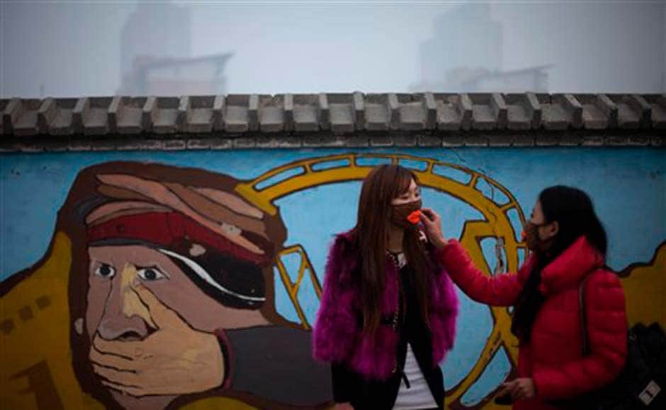 A woman helps adjust a mask for her friend outside an amusement park in Beijing: AP A woman helps adjust a mask for her friend outside an amusement park in Beijing: AP