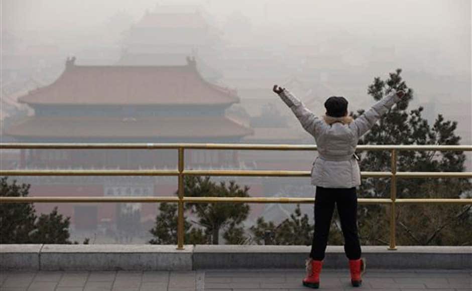 A visitor stretches her arms as she looks over the Forbidden City through severe haze in Beijing: AP A visitor stretches her arms as she looks over the Forbidden City through severe haze in Beijing: AP