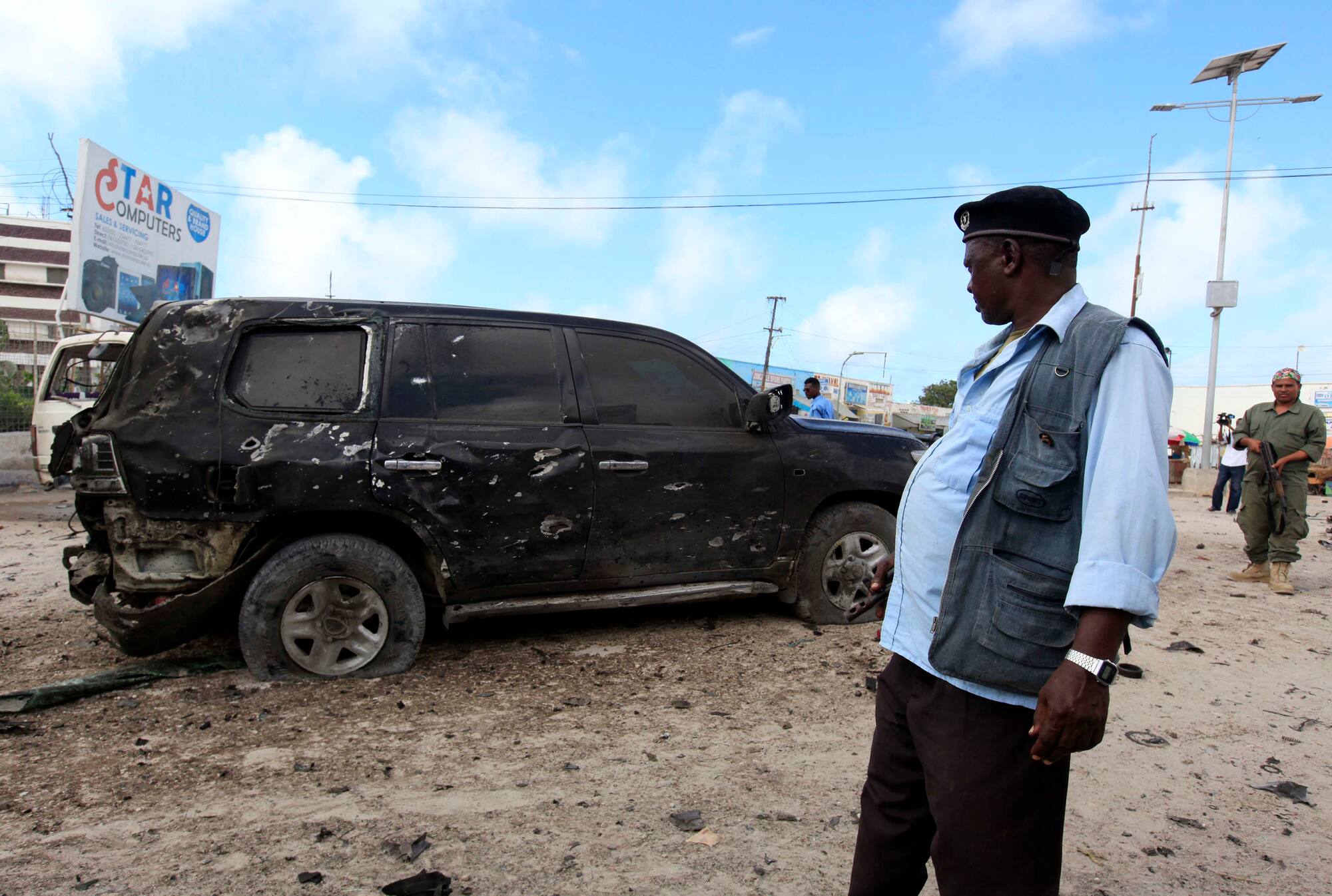 An officer stands by a wrecked car at the scene of car bomb explosion along the 