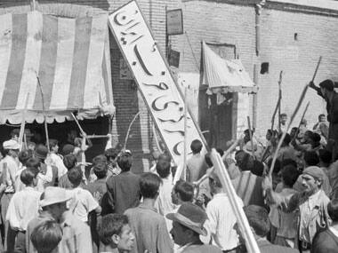 A crowd of demonstrators tears down the Iran Party's sign from the front of the headquarters in Tehran during the pre-Shah riot. AP