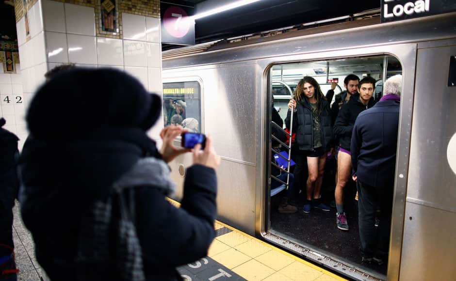 A woman takes a photograph of a group of people standing in the subway with no pants on during the annual 