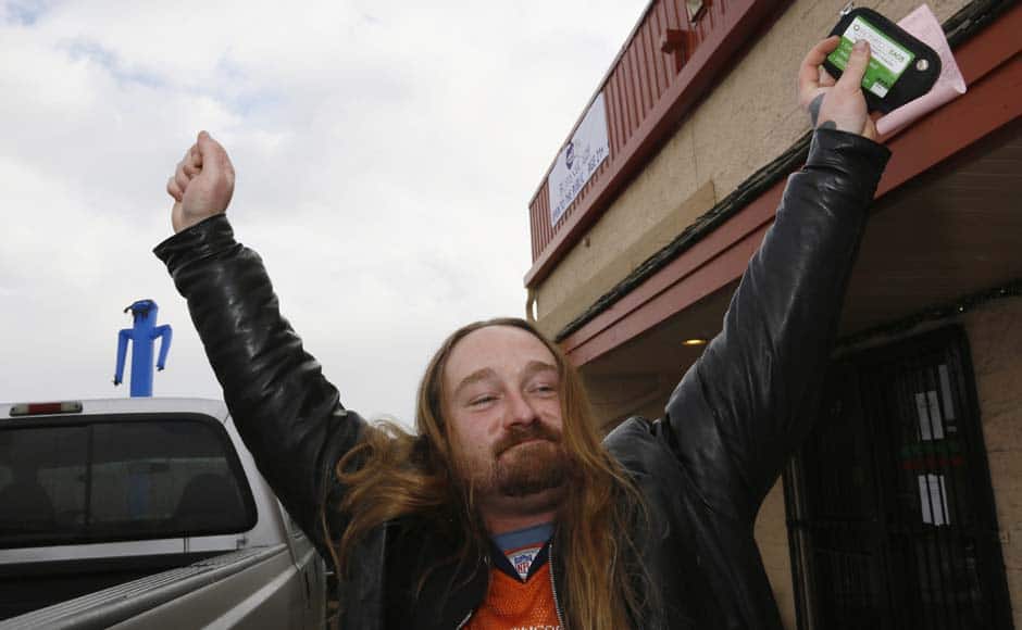 Jesse Phillips, wearing a Denver Broncos jersey, celebrates being the first person to legally buy recreational marijuana (in his left hand) at the BotanaCare store in Northglenn, Colorado January 1, 2014. Marijuana proprietors in Colorado are pioneers in a new chapter of America's drug culture that marks the first time cannabis will be legally produced, sold and taxed under a special system many states have long established for alcohol sales. REUTERS/Rick Wilking (UNITED STATES - Tags: BUSINESS SOCIETY POLITICS DRUGS) - RTX16Z81