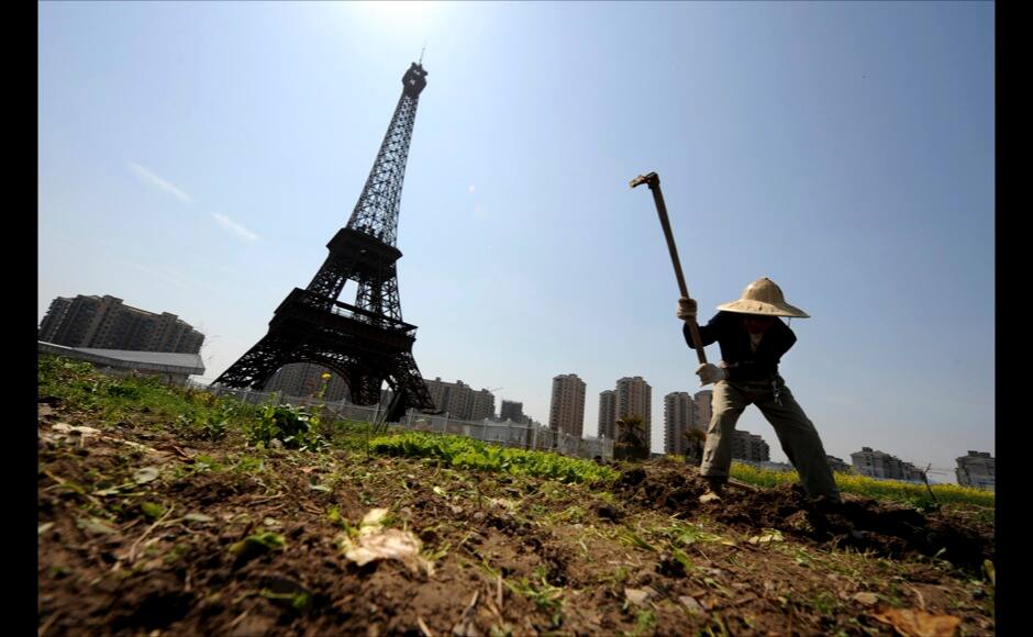 A farmer tills the field near the replica of the Eiffel Tower at the Tianducheng development in Hangzhou, Zhejiang province, March 21, 2014. REUTERS