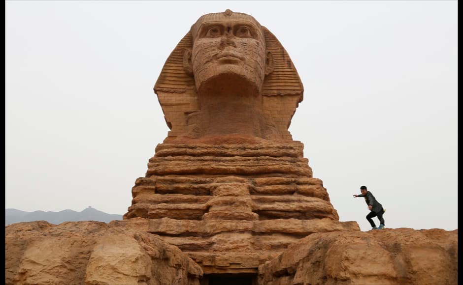 A man poses for photographs on a full-scale replica of the Sphinx, that is part of an unfinished theme park that will also accommodate the production of movies, television shows and animation, on the outskirts of Shijiazhuang, Hebei province May 10, 2014. The replica is a venue of a film studio which is already functioning. The theme park is scheduled to open this October, local media reported. Picture taken May 10, 2014. REUTERS