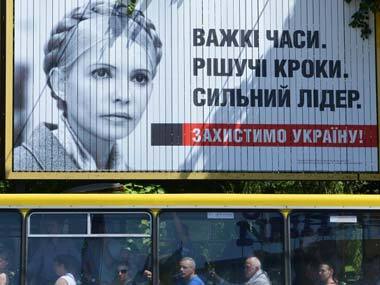 People ride a bus passing under a billboard depicting Ukrainian presidential candidate Yulia Tymoshenko reading 