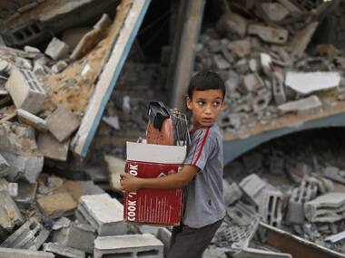 A Palestinian boy carries belongings as he walks past a house which was destroyed in an Israeli air strike in Gaza City. Reuters image