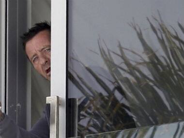 Phil Rudd, drummer for the rock band AC/DC, gestures from a window at his house in Tauranga, New Zealand. AP