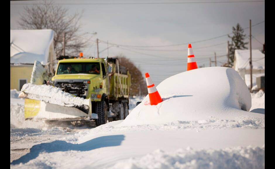 An abandon car marked by orange cones is buried under snow as a snowplow passes by in Buffalo, New York, November 19, 2014. Temperatures in all 50 U.S. states dipped to freezing or below on Tuesday as an unseasonably cold blast of weather moved across the country while heavy snow prompted a state of emergency in western New York and contributed to the deaths of four people. REUTERS