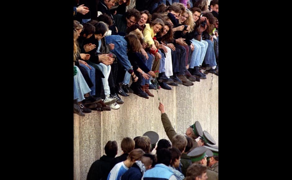 FILE PHOTO 10NOV89 - An East Berlin border guard hands a flower back to West Berlin citizens who are sitting atop the Berlin Wall in front of the Brandenburg Gate. Other West Berlin citizens mingle with border guards on the East Berlin side. November 9 marks the fifth anniversaryof the wall coming down - RTXF71Y