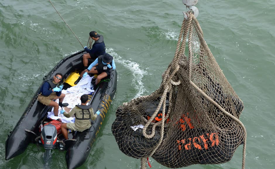 Indonesian Navy frogmen and underwater demolition unit personnel on a boat carrying bodies from AirAsia flight QZ8501, look as a body is lifted (unseen) to the Indonesian Navy vessel KRI Banda Aceh, at sea January 3, 2015. Ships searching for the wreck of an AirAsia passenger jet that crashed with 162 people on board have pinpointed two 
