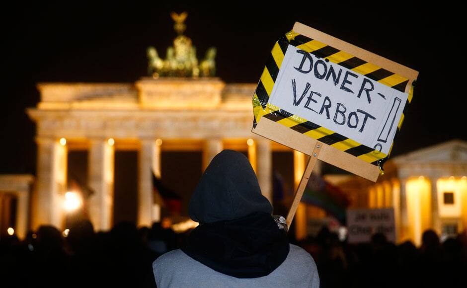 An anti-PEGIDA protester holds a placard reading 'Doner prohibition' as he stands behind members of BAERGIDA, Berlin's section of anti-immigration movement Patriotic Europeans Against the Islamisation of the West (PEGIDA) demonstrating in front of the Brandenburg Gate in Berlin January 12, 2015. REUTERS
