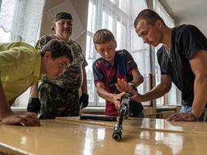 A pro-Russian rebel looks on as young boys learn to use a Kalashnikov machine gun. AFP 