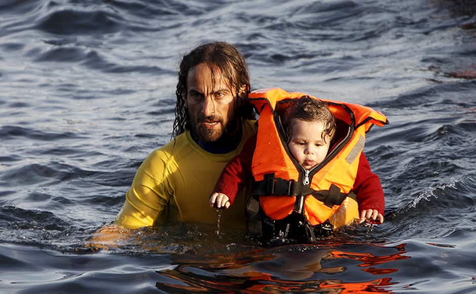 A volunteer lifeguard carries a baby as a half-sunken catamaran carrying around 150 refugees, most of them Syrians, arrives after crossing part of the Aegean sea from Turkey on the Greek island of Lesbos, October 30, 2015. There were no casaulties amongst the refugees who were travelling on the catamaran, according to a Reuters witness. The death toll from drownings at sea has mounted recently as weather in the Aegean has taken a turn for the worse, turning wind-whipped sea corridors into deadly passages for thousands of refugees crossing from Turkey to Greece. REUTERS/Giorgos Moutafis
