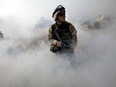 A soldier stands guard in a haze of smoke outside a building during a cordon and search operation in a neighbourhood near the Baghdad suburb of al Sadr City August 15, 2004. Photographer David P. Gilkey. Reuters