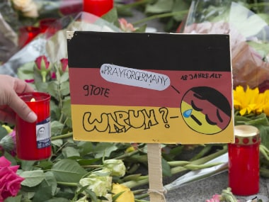 A woman lights a candle besides a sign painted in the colors of German flag besides the Olympia shopping center in Munich on Saturday. The word down reads: 'Why?'. AP
