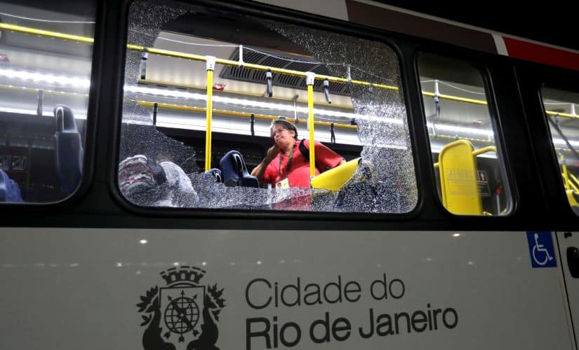 A member of the media stands near a shattered window on a bus in the Deodoro area of Rio de Janeiro. AP