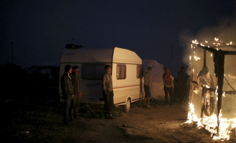 Migrants watch as tents in the Calais camp are burnt by authorities. AP