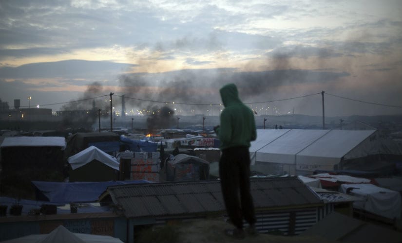 A migrant looks at the burning Calais camp. AP