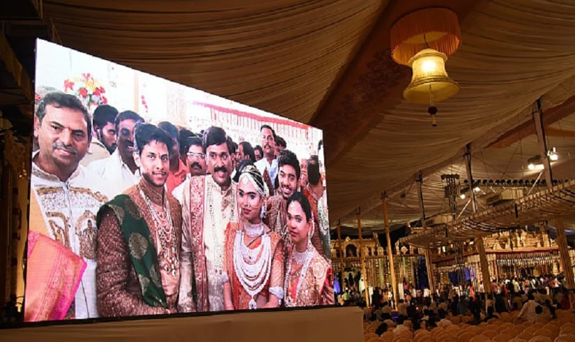 Indian mining tycoon, Gali Janardhan Reddy, (C) is seen on a big screen as he poses with his daughter Bramhani (2R) and son-in-law, Rajeev Reddy (2L) during their wedding in Bengaluru. Getty Images.