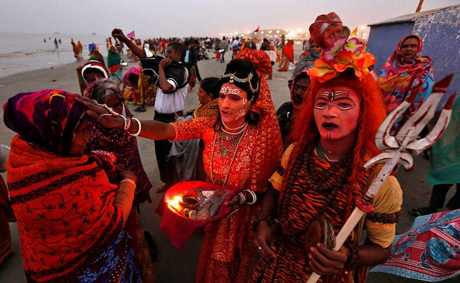 Two men dressed as Hindu Lord Shiva (R) and Goddess Parvati (C) give blessings to a pilgrim at the confluence of the river Ganges and the Bay of Bengal, ahead of the Two men dressed as Hindu Lord Shiva (R) and Goddess Parvati (C) give blessings to a pilgrim at the confluence of the river Ganges and the Bay of Bengal, ahead of the