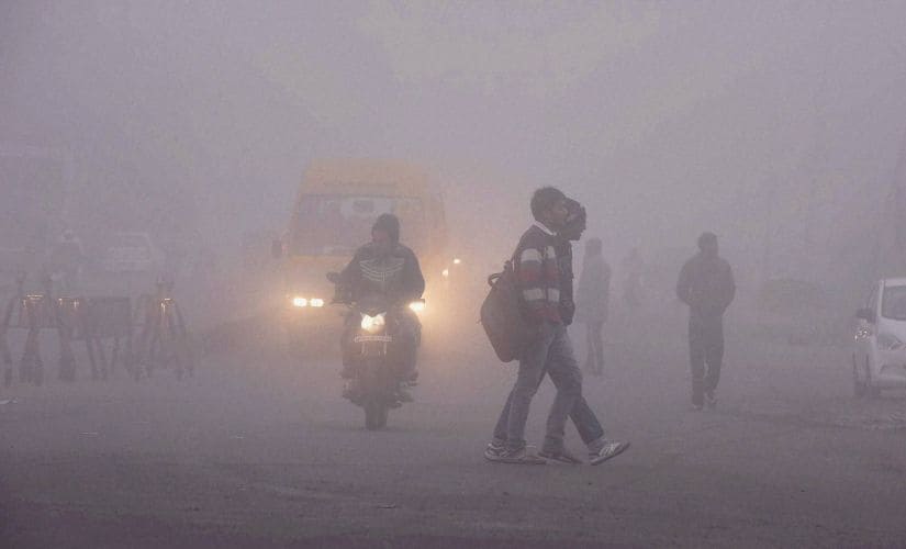 People and vehicles move through a thick blanket of fog in Bhopal on Monday. PTI