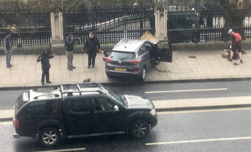 People stand near a crashed car and an injured person lying on the ground, right, on Bridge Street near the Houses of Parliament in London. AP