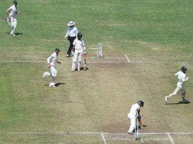 Indian captain Virat Kohli looks back at his stumps as Australian cricketers celebrate on Day 3 of the Pune Test. AFP