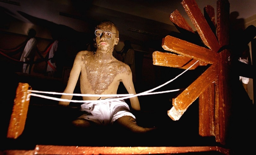 An Indian college student, smeared with clay to resemble Mahatma Gandhi, sits beside a spinning wheel during an event to mark the 55th anniversary of the death of Gandhi in Bombay January 30, 2003. Students from a city college reenacted several scenes from Gandhi's freedom struggle against the British colonial rule. The day is observed as 'Martyr's Day' in the country. REUTERS/Arko Datta AD/CP - RTRHG9P