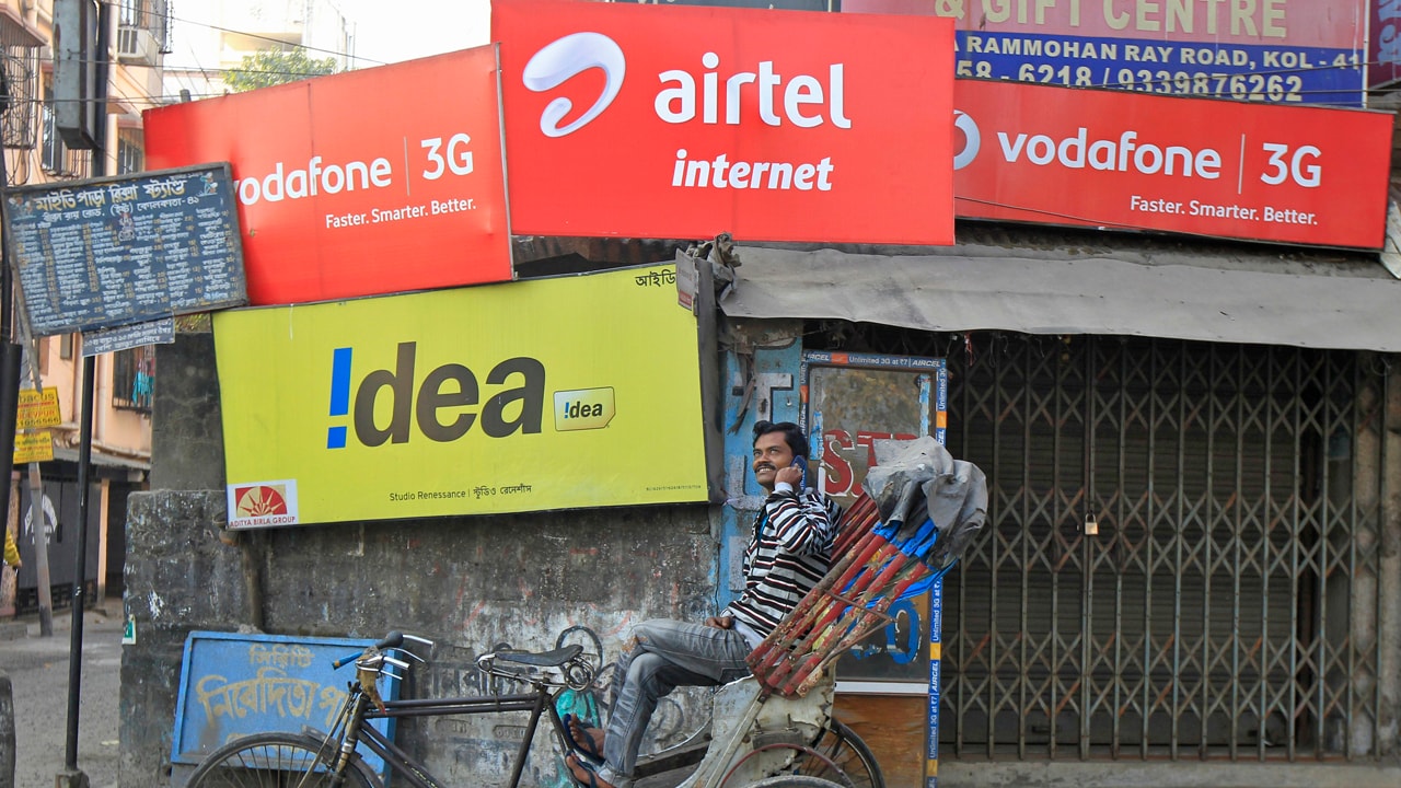 A rickshaw puller speaks on his mobile phone as he waits for customers in front of advertisement billboards belonging to telecom companies in Kolkata February 3, 2014. India is auctioning airwaves in both the 1800 megahertz and 900 megahertz bands, and Reliance Industries, a formidable rival to market leaders Bharti Airtel Ltd and Vodafone Group PLC, has unexpectedly opted to compete for both, sources have said. Spectrum in the 1800 Mhz range would enable Reliance to offer voice services and improved coverage for its 4G Internet service and bidding for the spectrum is expected to be relatively modest given that there is plenty of it and it is less efficient than the 900 Mhz bandwidth. Picture taken February 3, 2014. REUTERS/Rupak De Chowdhuri (INDIA - Tags: BUSINESS TELECOMS) - RTX186ZH