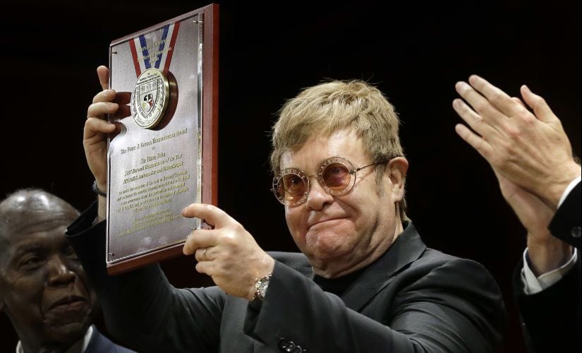 Musician Elton John holds up the 2017 Harvard Humanitarian of the Year Award after being presented with the award Monday, Nov. 6, 2017, during ceremonies at Harvard University, in Cambridge, Mass. Elton John was recognized during the ceremonies for his work in combating HIV/AIDS around the world. (AP Photo/Steven Senne)