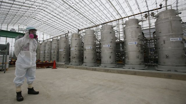 A Tokyo Electric Power Co. (TEPCO) official wearing a radioactive protective gear stands in front of Advanced Liquid Processing Systems during a press tour at the Fukushima Dai-ichi nuclear power plant. Image: AP