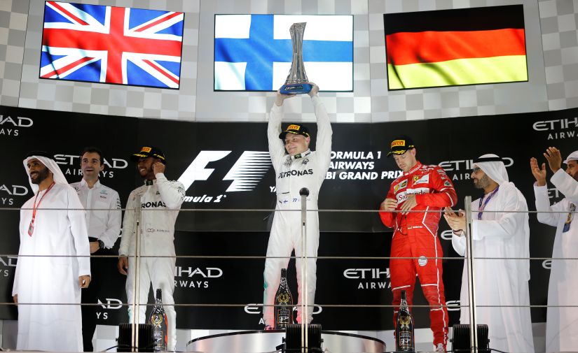 Mercedes' Valtteri Bottas celebrates with the trophy after winning the Abu Dhabi Grand Prix as Mercedes' Lewis Hamilton and Ferrari's Sebastian Vettel look on. Reuters