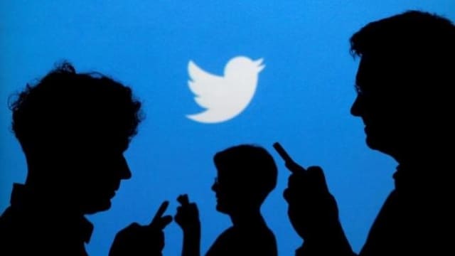 People holding mobile phones are silhouetted against a backdrop projected with the Twitter logo in this illustration picture taken. Image: Reuters