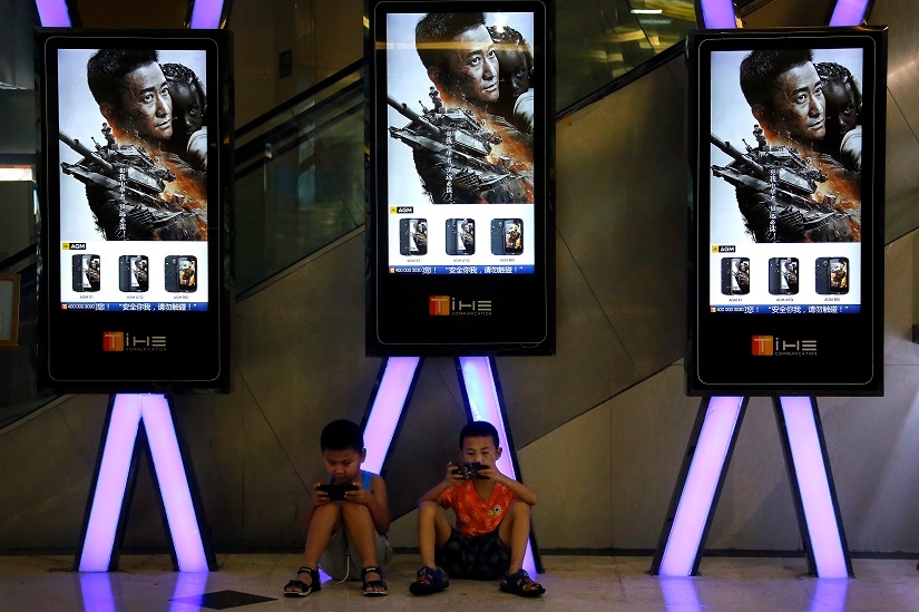 FILE - In this Aug. 10, 2017, file photo, children use smartphones near monitors displaying Chinese action movie "Wolf Warrior 2" at a cinema in Beijing. China's total domestic movie ticket sales rose 13.5 percent in 2017 to 55.9 billion yuan ($8.6 billion), a state news agency said Monday, Jan. 1, 2018. The top-grossing title was the mainland-made action picture "Wolf Warrior 2," which took in 5.7 billion yuan ($875 million), the Xinhua News Agency said, citing data from the State Administration of Press, Publication, Radio, Film and Television. (AP Photo/Andy Wong, File)