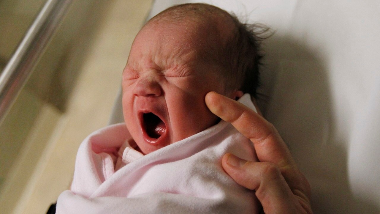 A newborn baby girl yawns as she is held by her father, shortly after being born at a hospital. Reuters